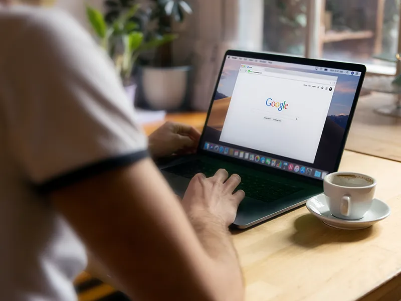 werbeagentur Berlin | Ein Mann genießt eine Tasse Kaffee und arbeitet mit seinem Laptop im Café. Auf dem Bildschirm ist eine Google-Suche geöffnet.